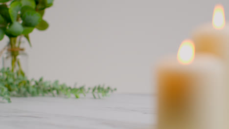 Still-Life-Of-Lit-Candles-With-Green-Leaved-Plant-On-Bright-Background-As-Part-Of-Relaxing-Spa-Day-Decor